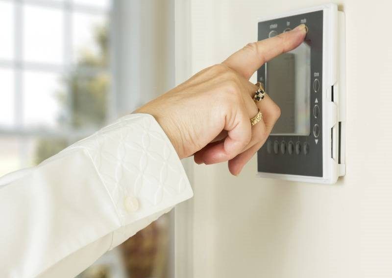Hand pressing a thermostat button on a white wall Hand pressing a thermostat button on a white wall