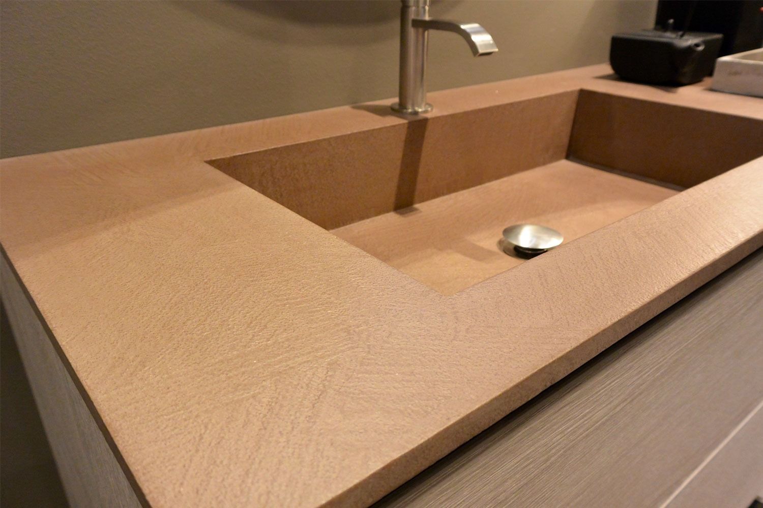 Lavabo rettangolare color beige con rubinetto e piletta cromati, integrato in un moderno piano d'appoggio.