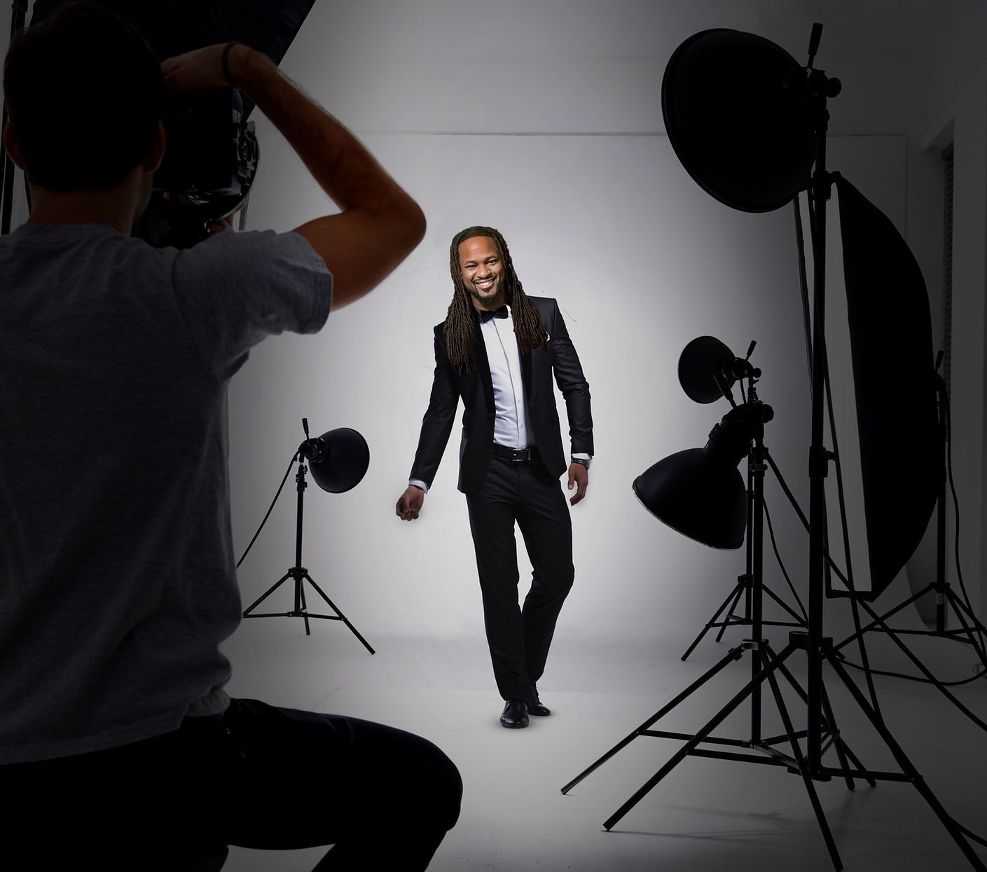 Photographer taking a photo of a man in a tuxedo, smiling in a studio with lights.