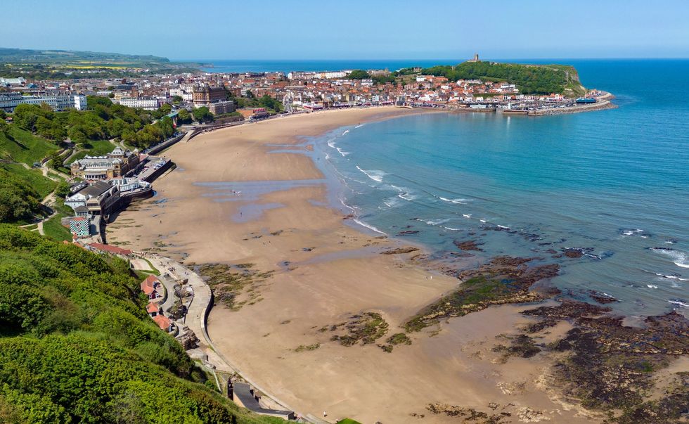 Wide sandy bay beside Scarborough, with blue sea, rocky shoreline, and green cliffs