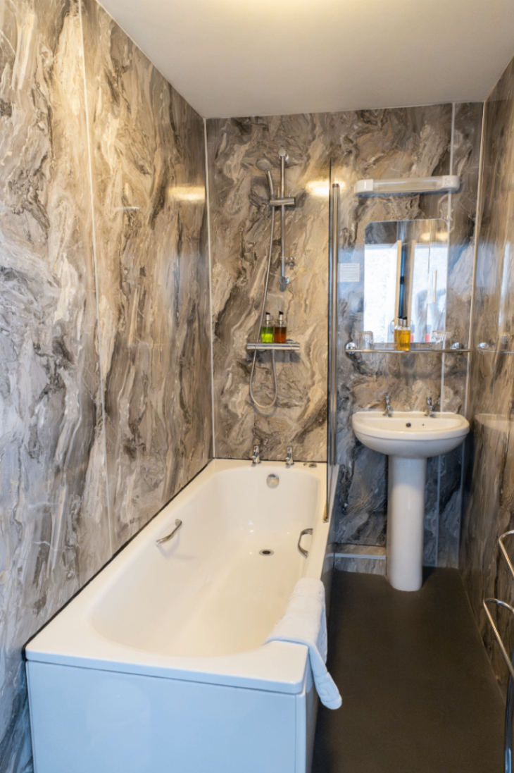 Small bathroom with marbled walls, a bathtub, and a pedestal sink beside a window.