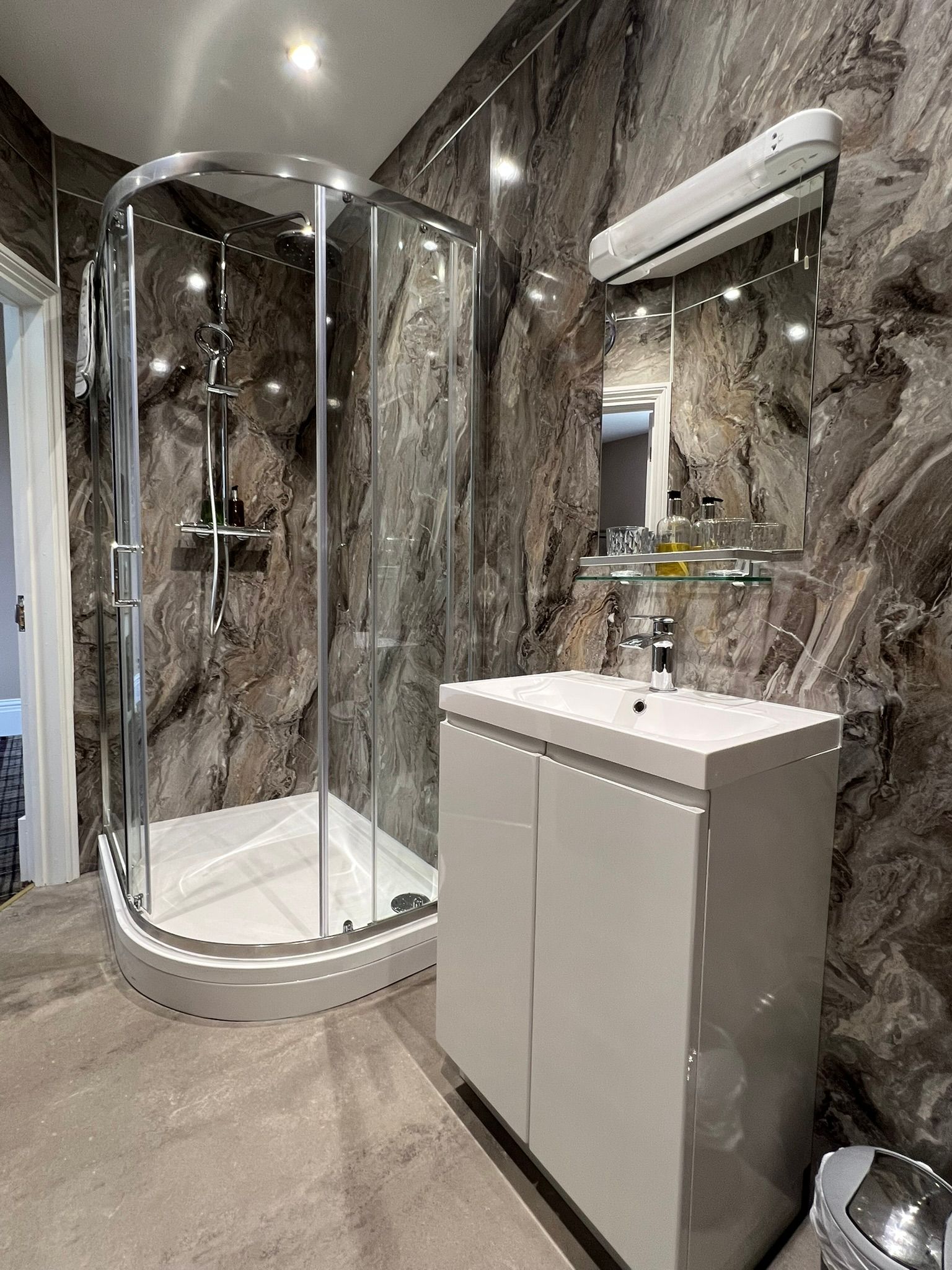 Modern bathroom with glass shower, marble walls, and white vanity sink
