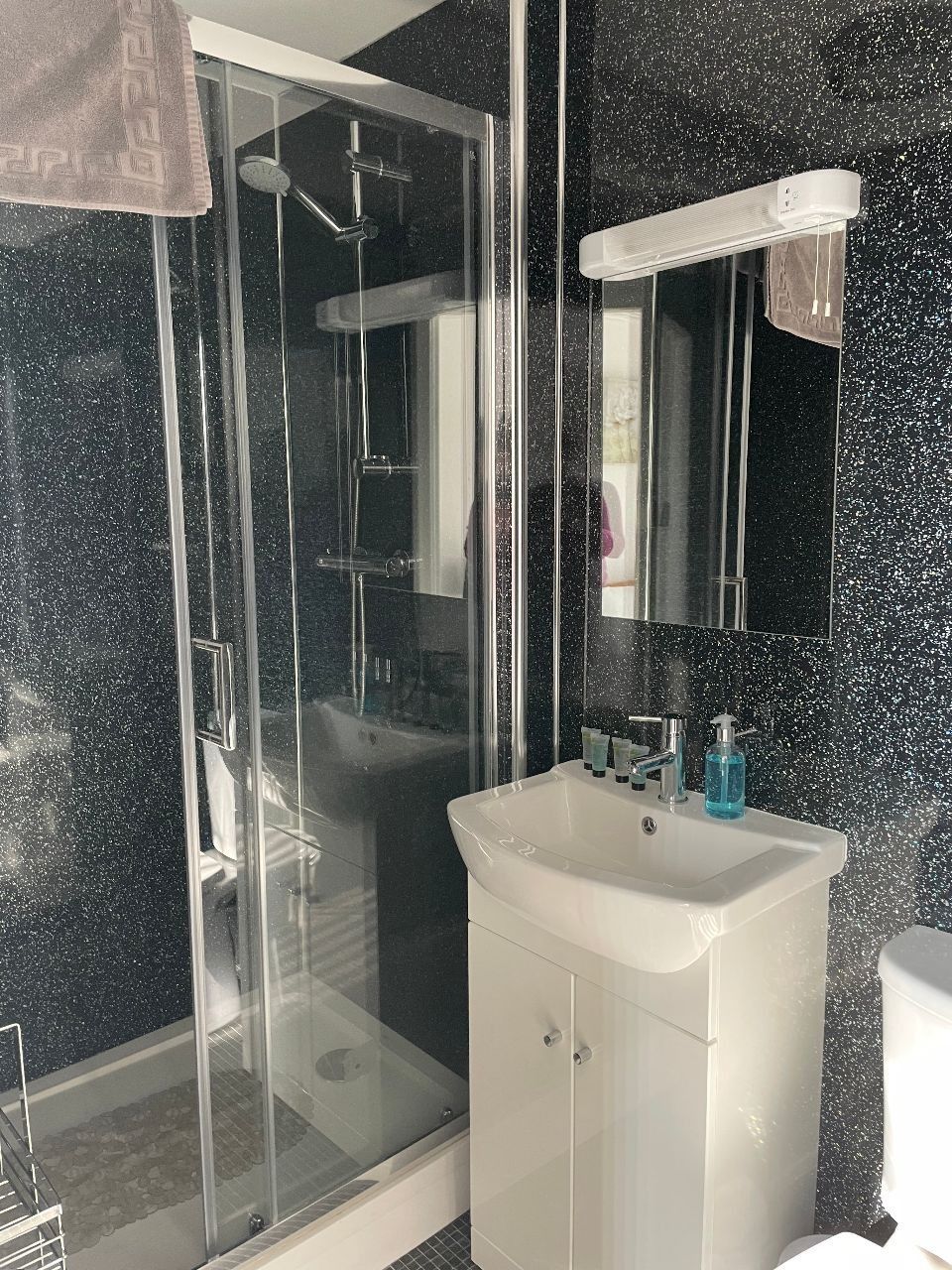 Small bathroom with glass shower, black speckled walls, and a white sink cabinet.