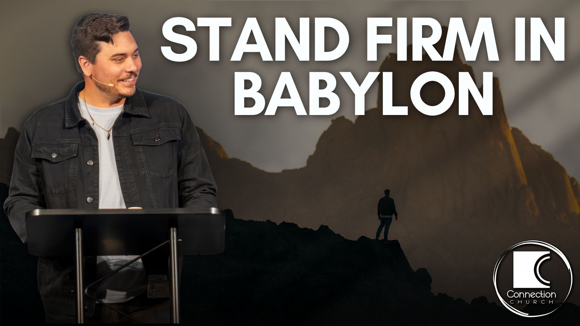 Man standing at a podium before a mountain backdrop with text: “STAND FIRM IN BABYLON”