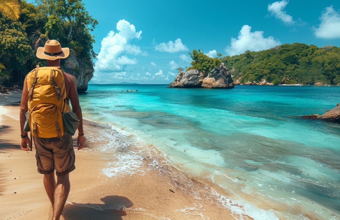 Turista caminhando por uma praia tropical com água turquesa, palmeiras e ilhas rochosas ao longe.