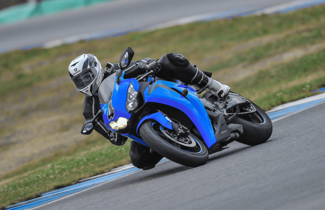 Motocicleta esportiva azul inclinada em uma curva acentuada em uma pista de corrida, piloto com equipamento completo de proteção.