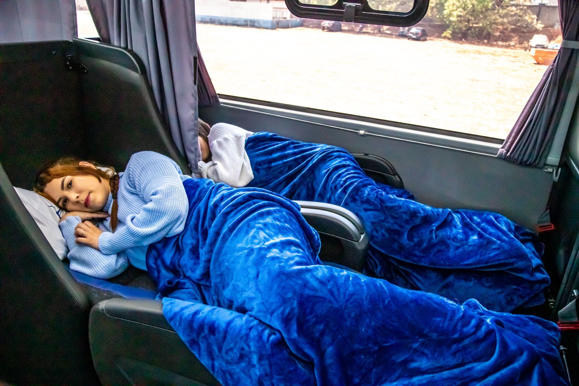 Duas pessoas dormindo sob cobertores azuis no banco de trás de um carro.