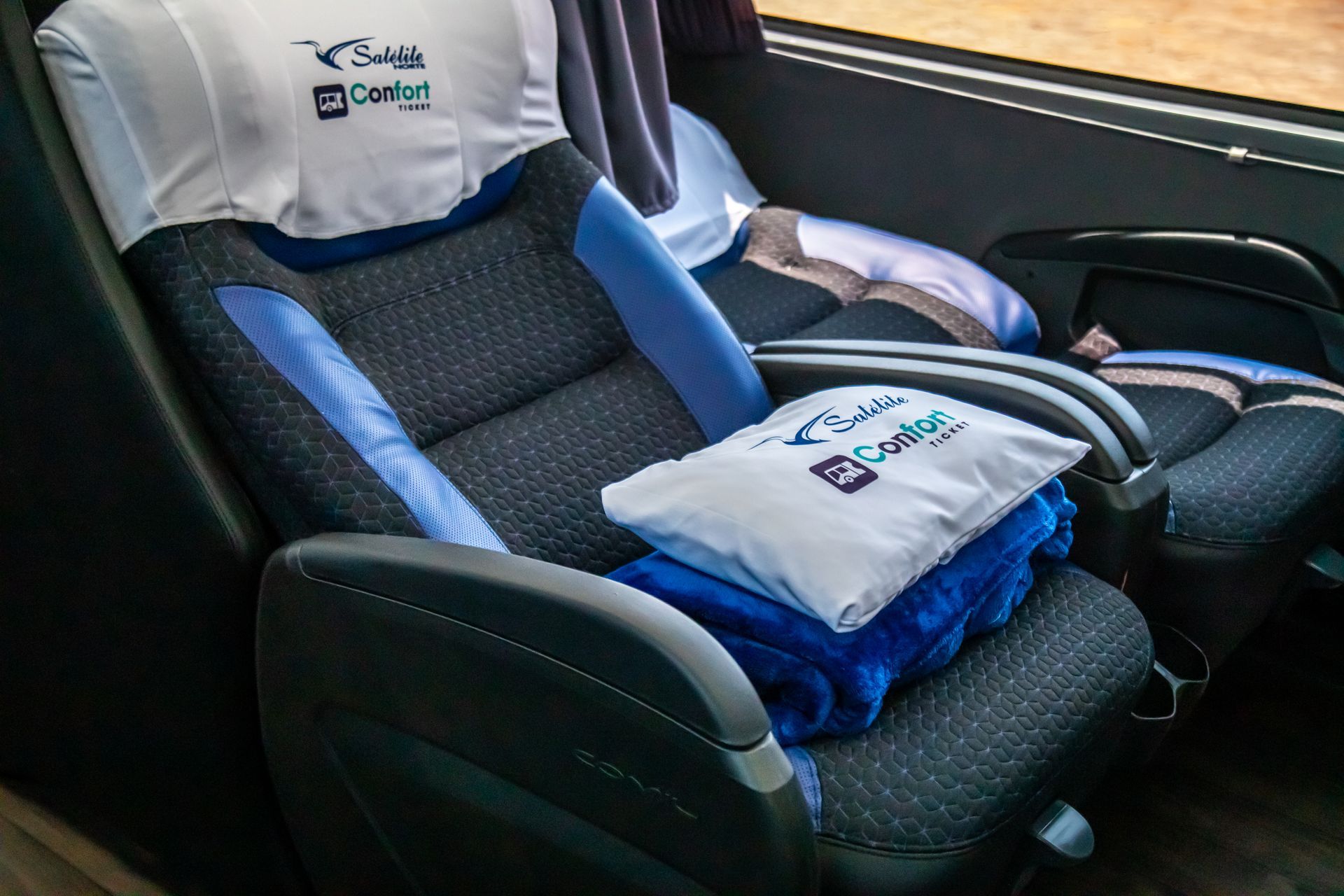 Cadeirinha de carro com almofadas e travesseiros azuis e pretos, colocada ao lado da janela do carro.