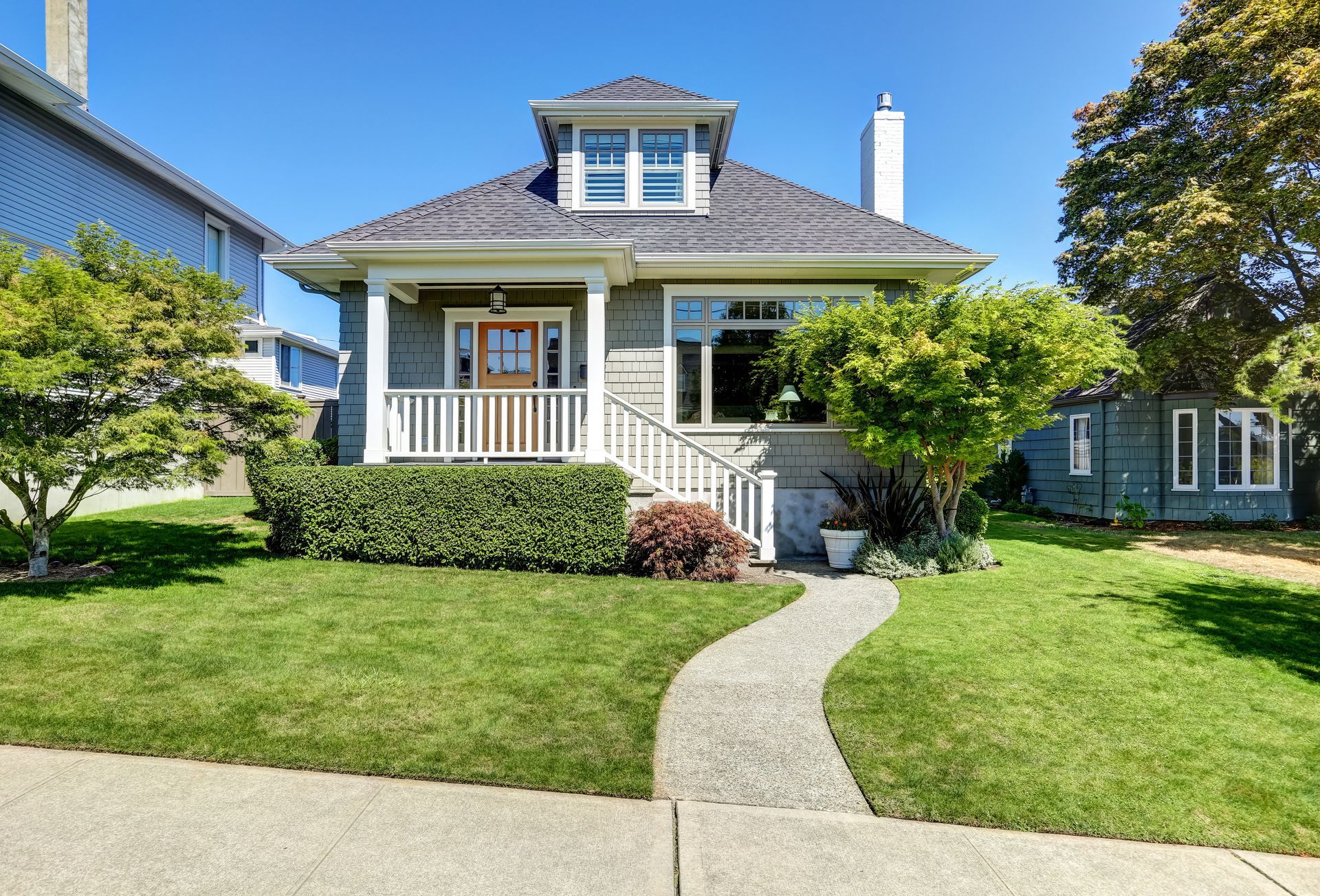 Gray house with white porch and walkway, lush green lawn, bright blue sky.