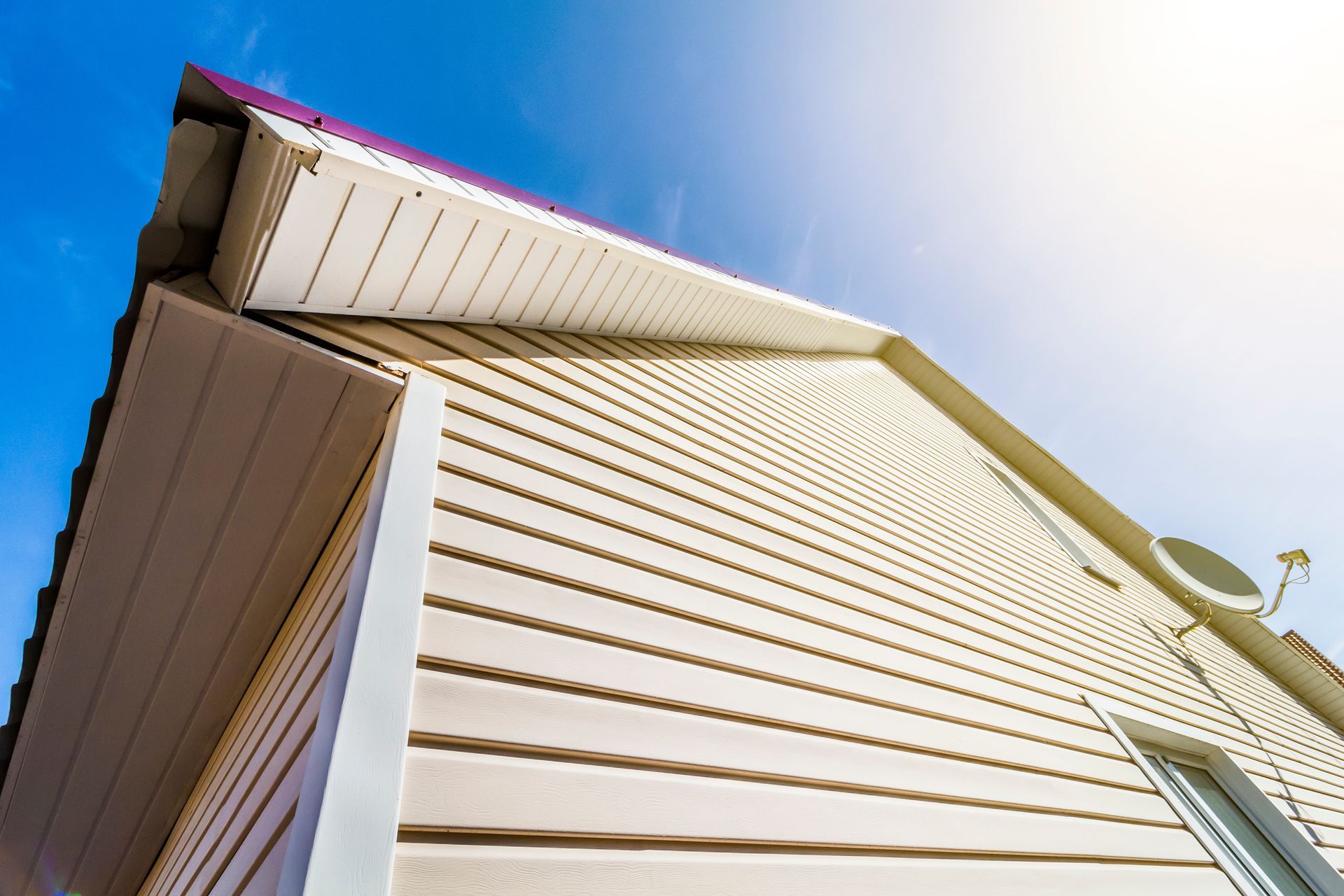 Beige vinyl siding on a house against a blue sky. Beige vinyl siding on a house against a blue sky.
