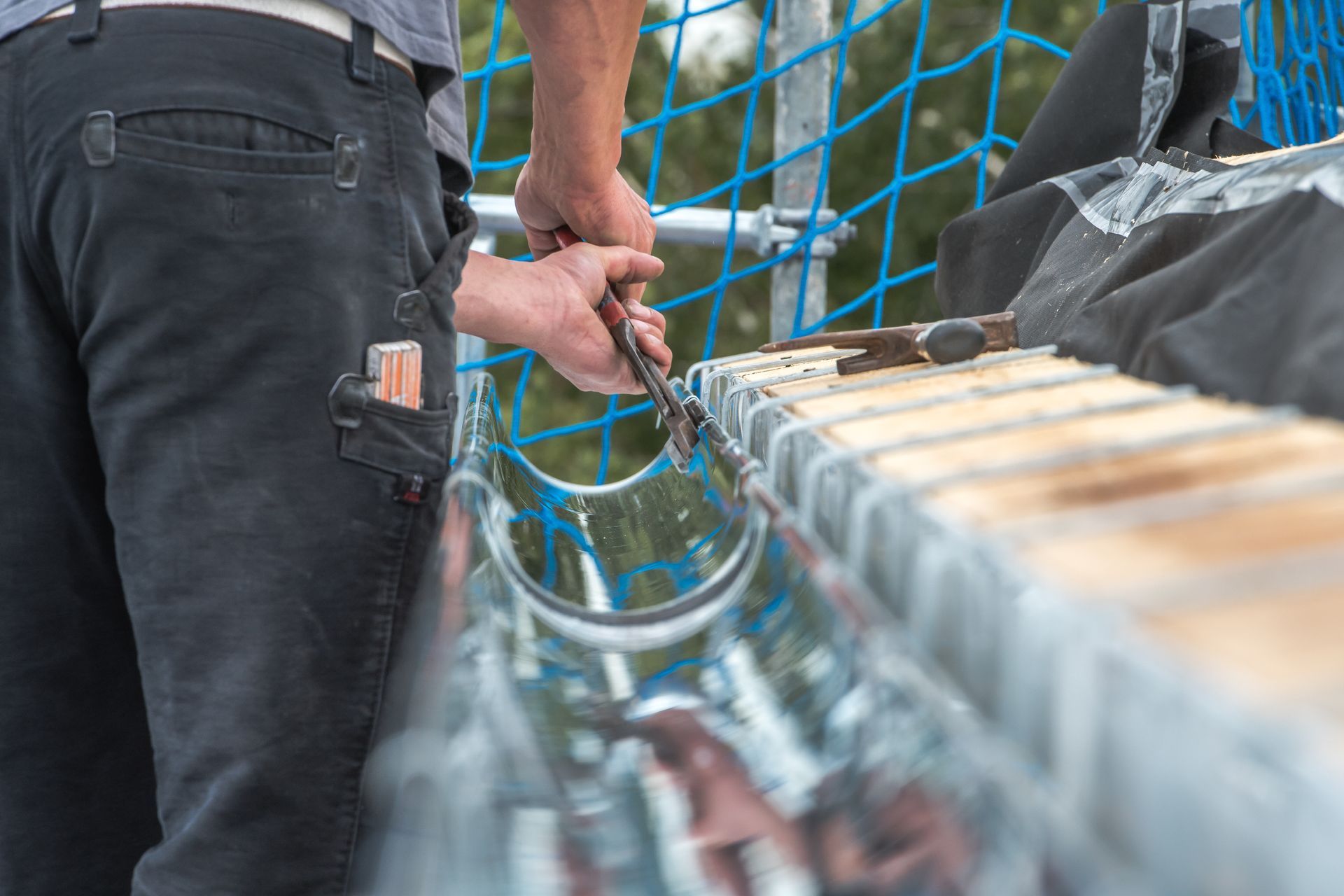 Person using pliers to work on a metal gutter on a building's edge. Person using pliers to work on a metal gutter on a building's edge.