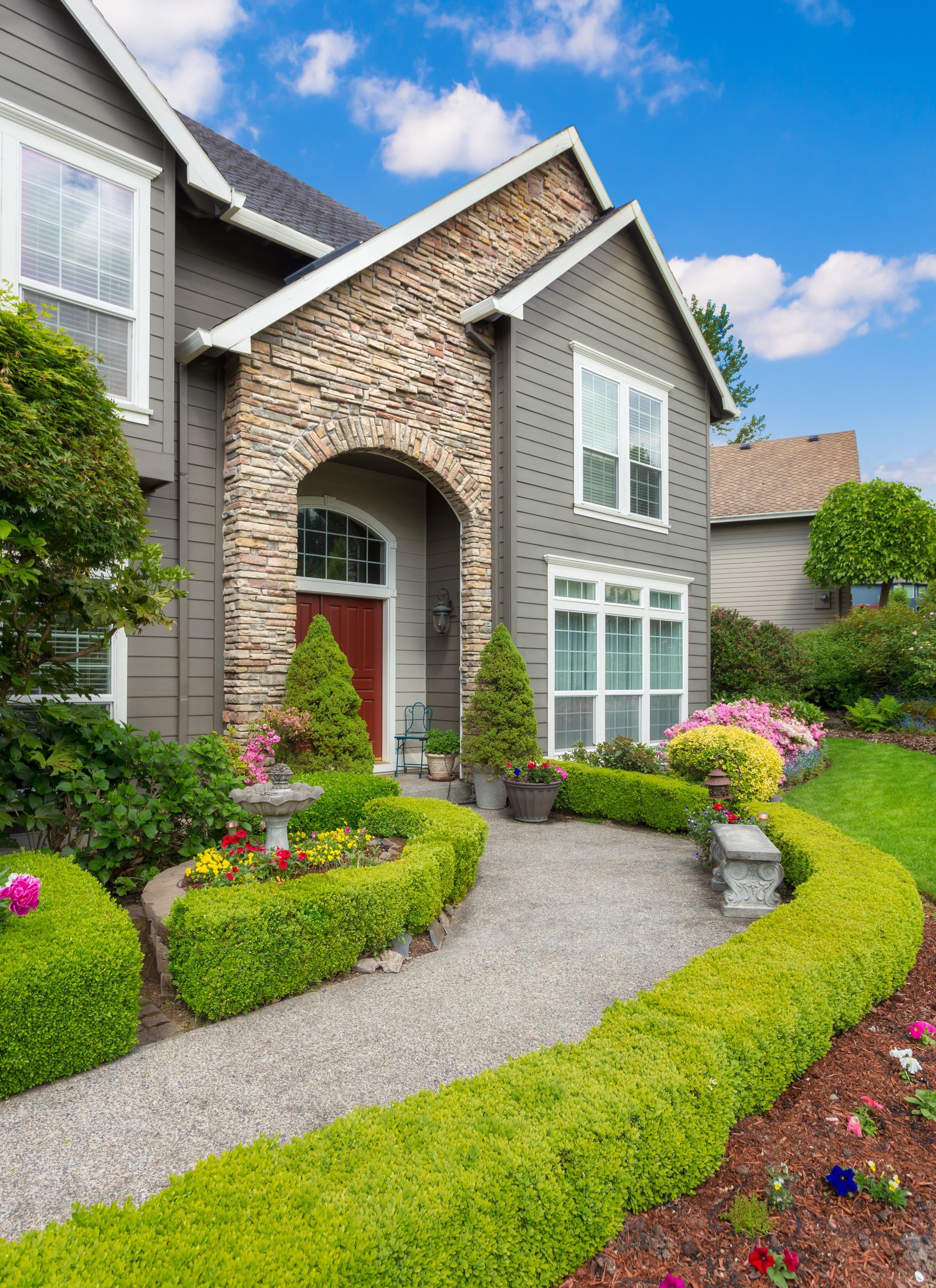 Gray house with a stone entryway, green lawn and hedges, and a gravel walkway. Gray house with a stone entryway, green lawn and hedges, and a gravel walkway.