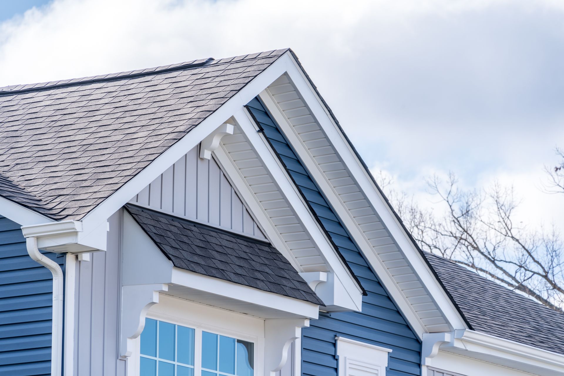 Blue house exterior with dark gray roof and white trim under a cloudy sky. Blue house exterior with dark gray roof and white trim under a cloudy sky.