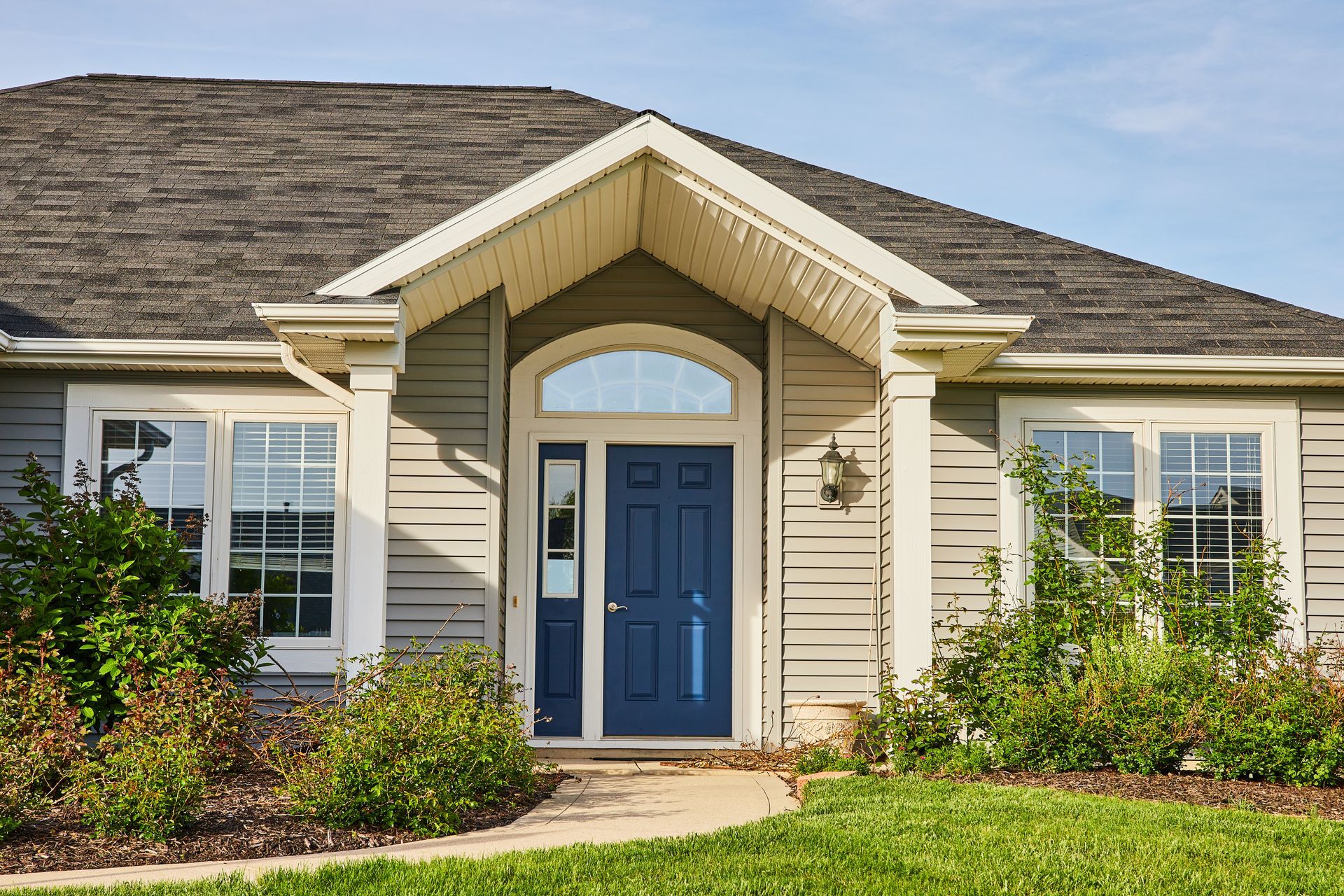 Blue front door of a gray-sided house with white trim, set in a green yard with a path. Blue front door of a gray-sided house with white trim, set in a green yard with a path.