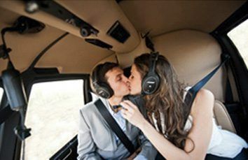 Couple kissing inside a helicopter, both wearing headsets and seatbelts.