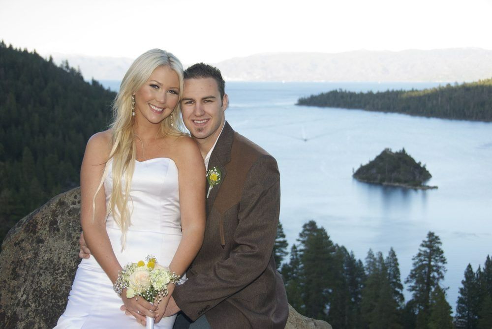 Couple in wedding attire smiling, overlooking lake with island.