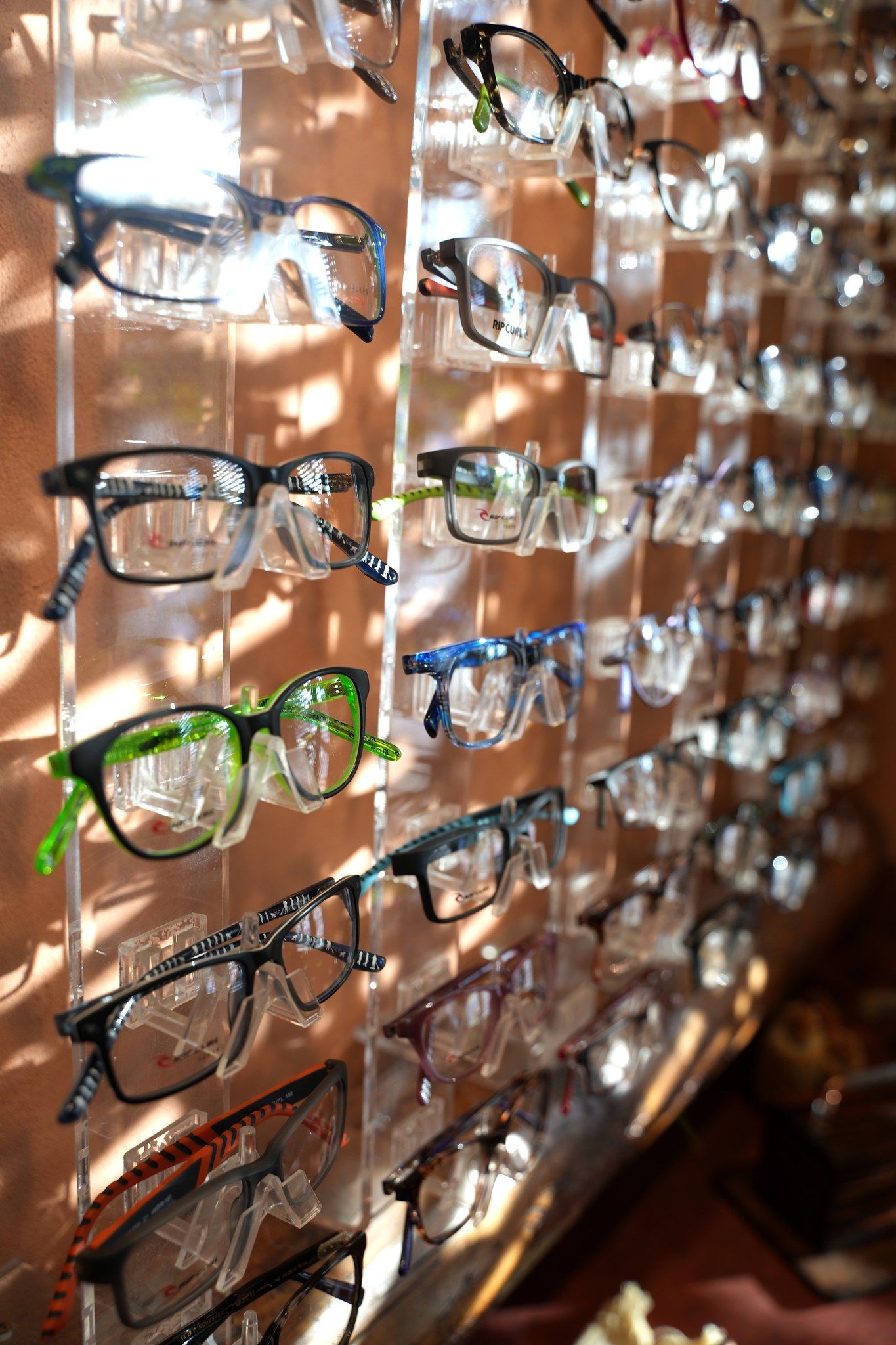 Rows of eyeglasses in various colors displayed on a store wall