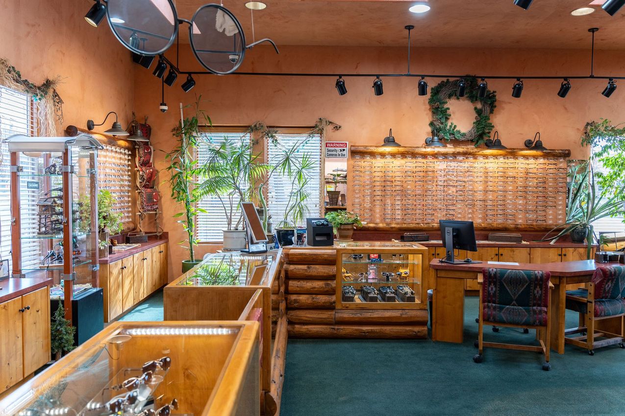 Wood-paneled retail shop with glass display cases, wicker baskets, and large windows filled with plants