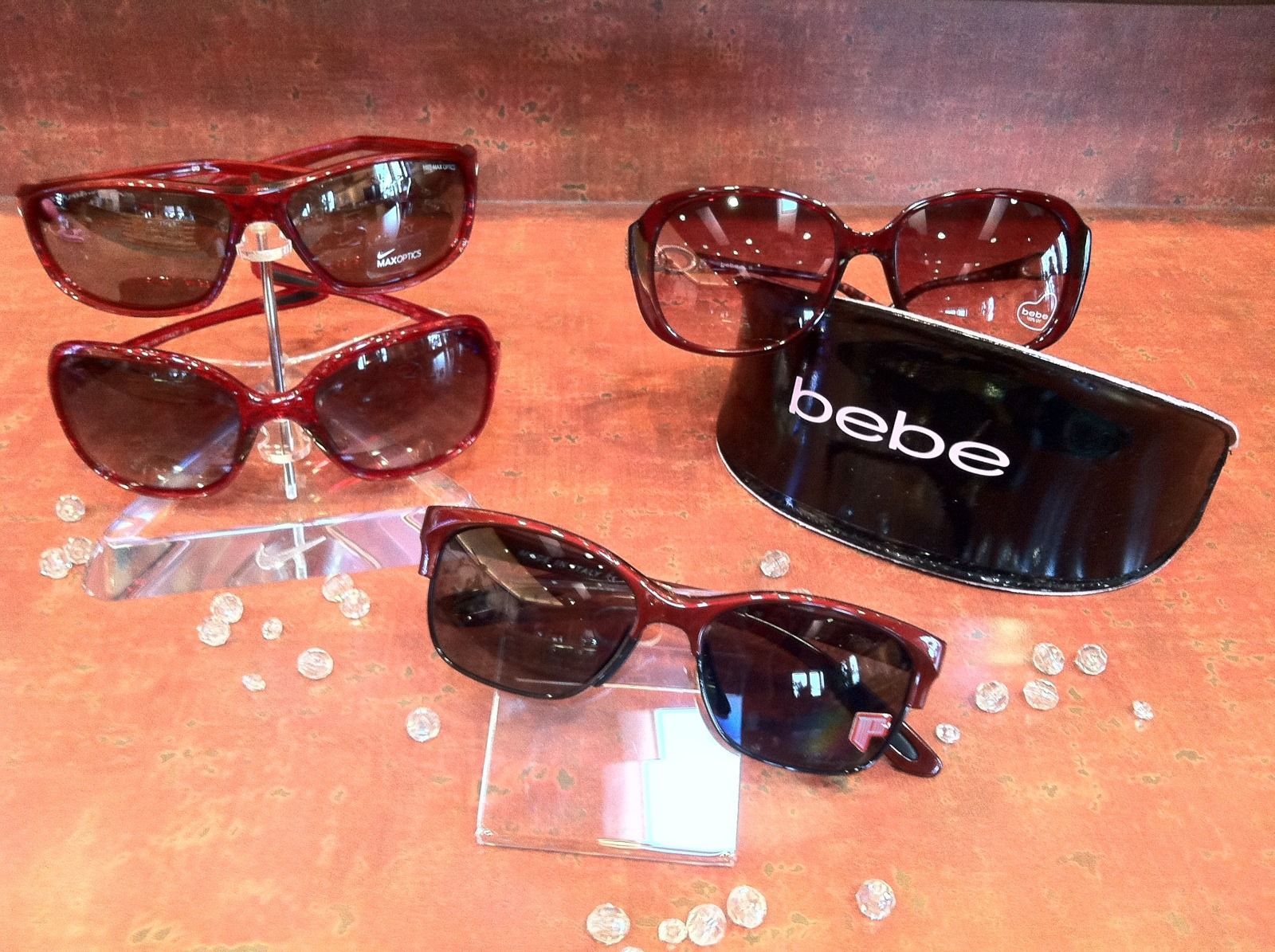Four pairs of sunglasses displayed on a wooden surface, including one black pair with “bebe” on the lens.