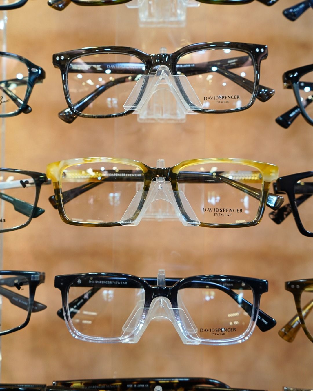 Display of eyeglass frames in black, gold, and clear on a wooden rack.