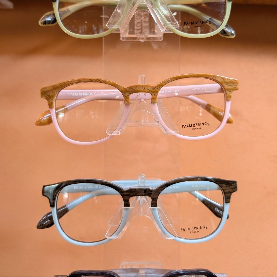 Three eyeglass frames in clear, gold, and black arranged vertically on an orange surface