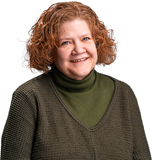 Smiling person with curly red hair wearing a green turtleneck and brown sweater on a white background