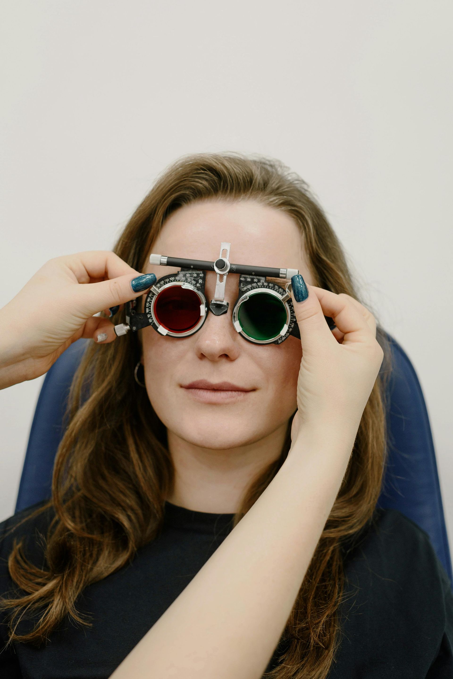 Person adjusting round eyeglasses with blue lenses on their face against a plain background