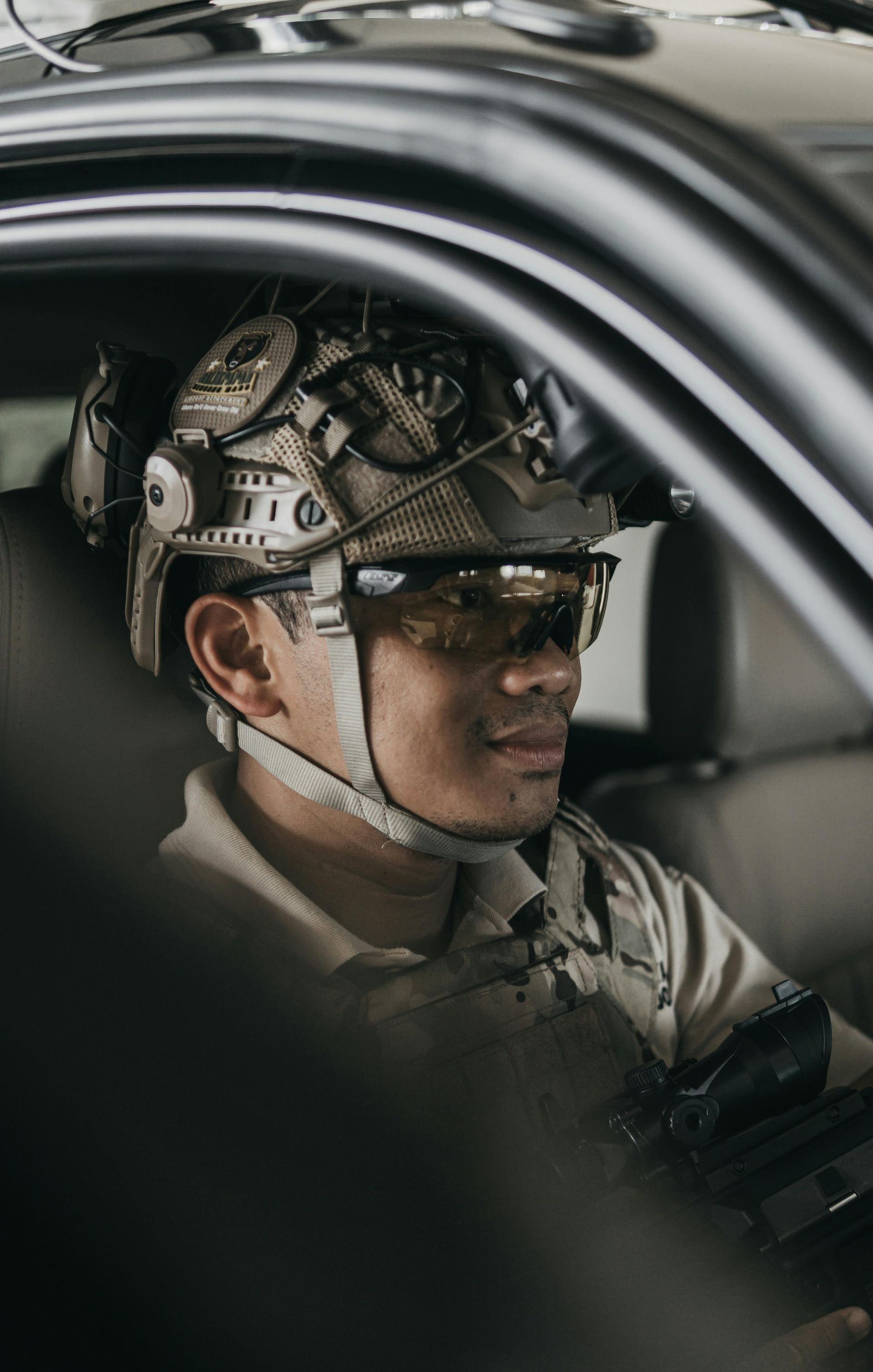 Person wearing a helmet and glasses sits inside a car, seen through the window.