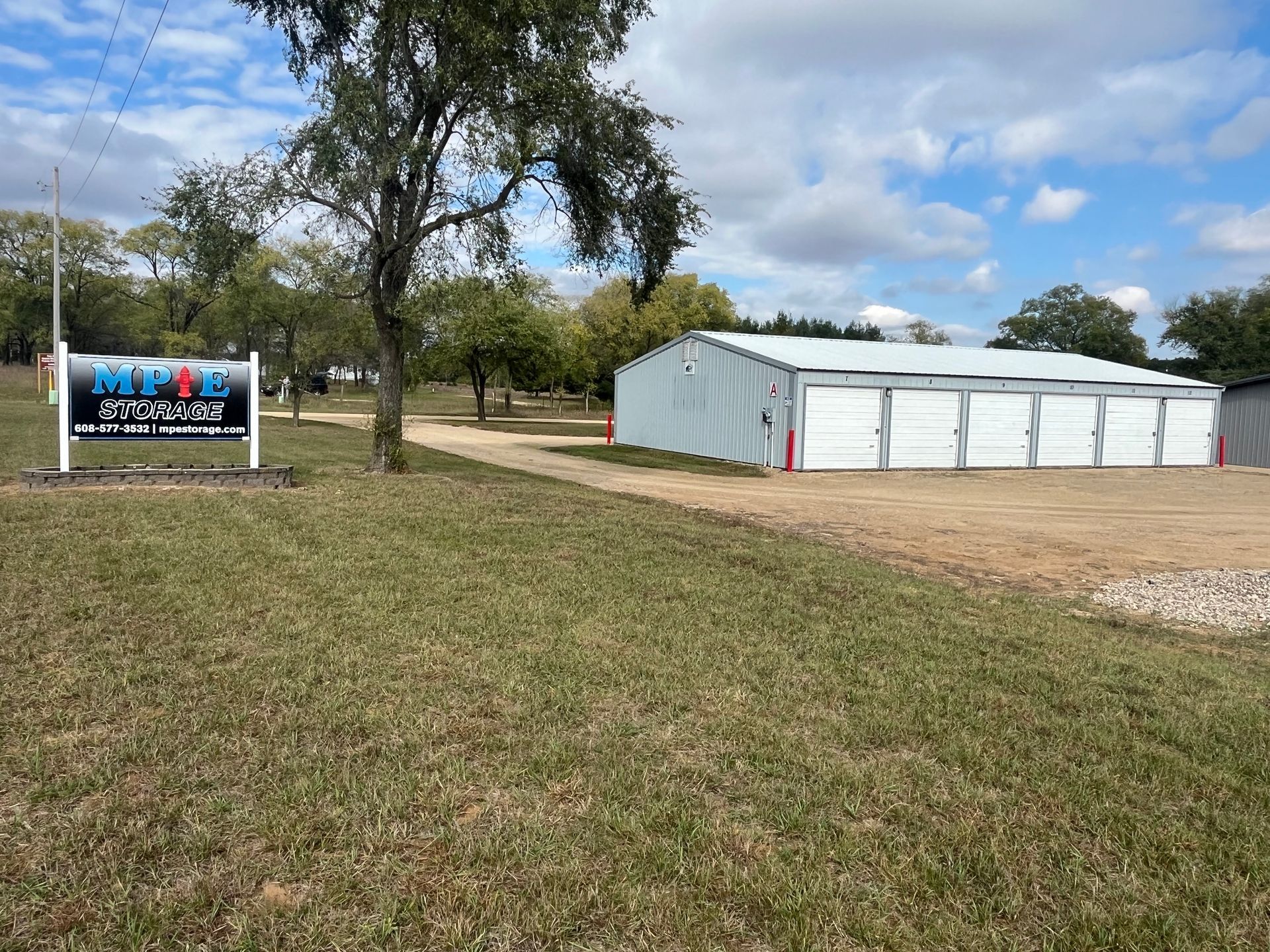 Storage facility with white units, sign, and grassy area under a partly cloudy sky.