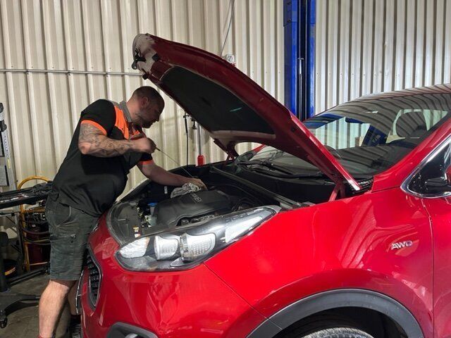 A Man Is Working on The Engine of A Red Car in A Garage — Steve Purse Automotive In Huskisson, NSW
