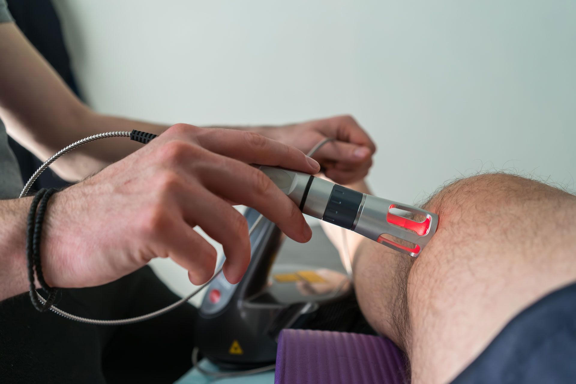 Person administering laser therapy to a knee in a medical setting. Red laser light visible.