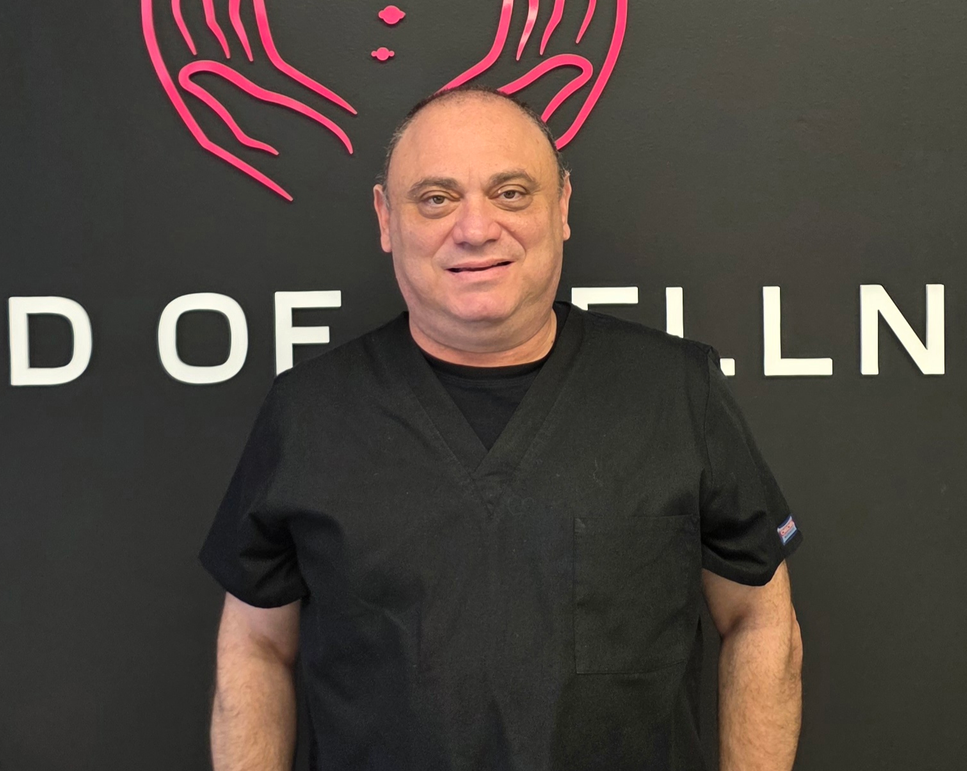 Man in black scrubs stands in front of a sign with a pink hand graphic.