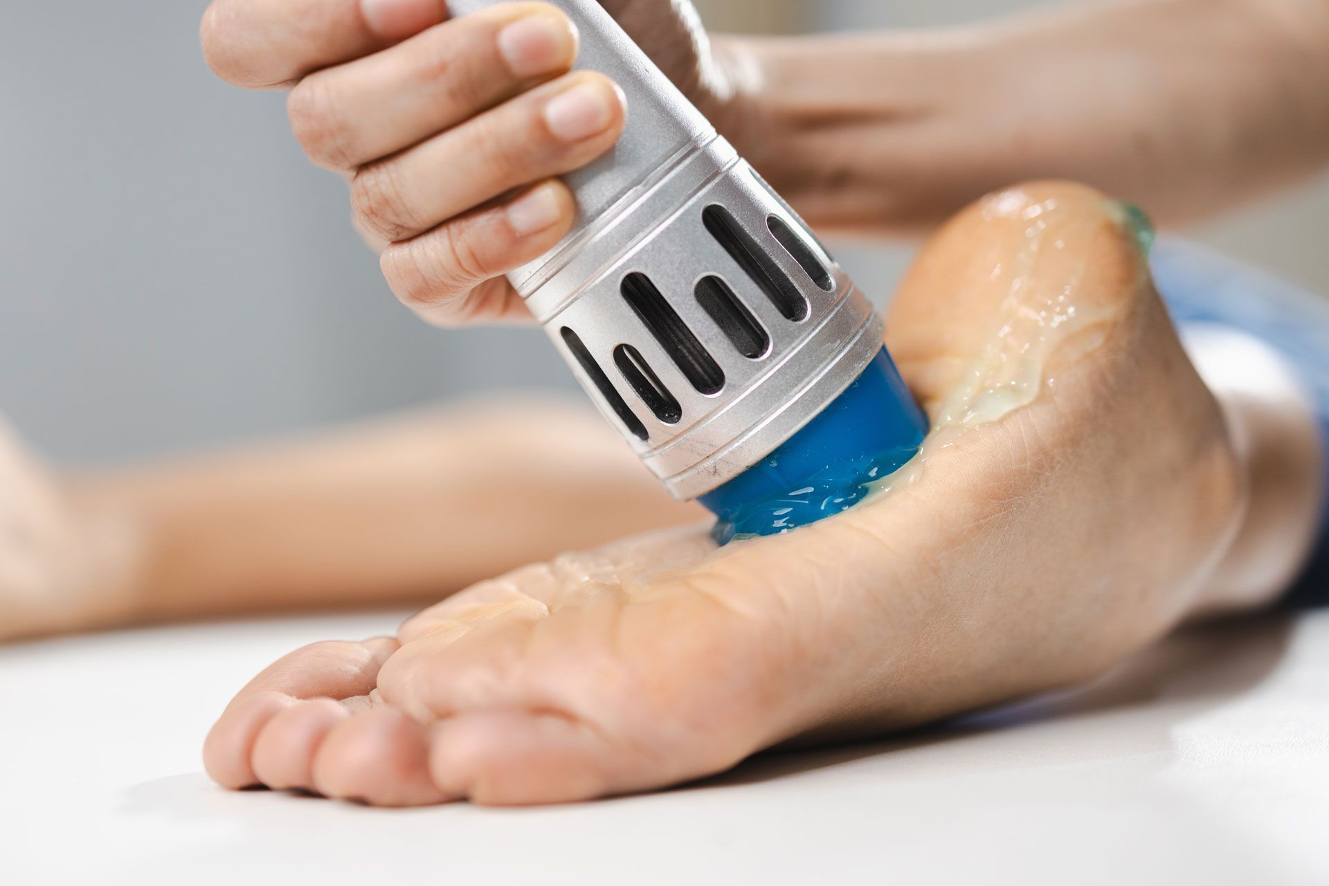 Foot being treated with ultrasound device; blue gel visible.