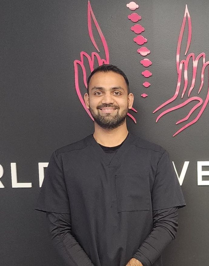 Man smiling, wearing black scrubs, in front of logo with hands and spine illustration.