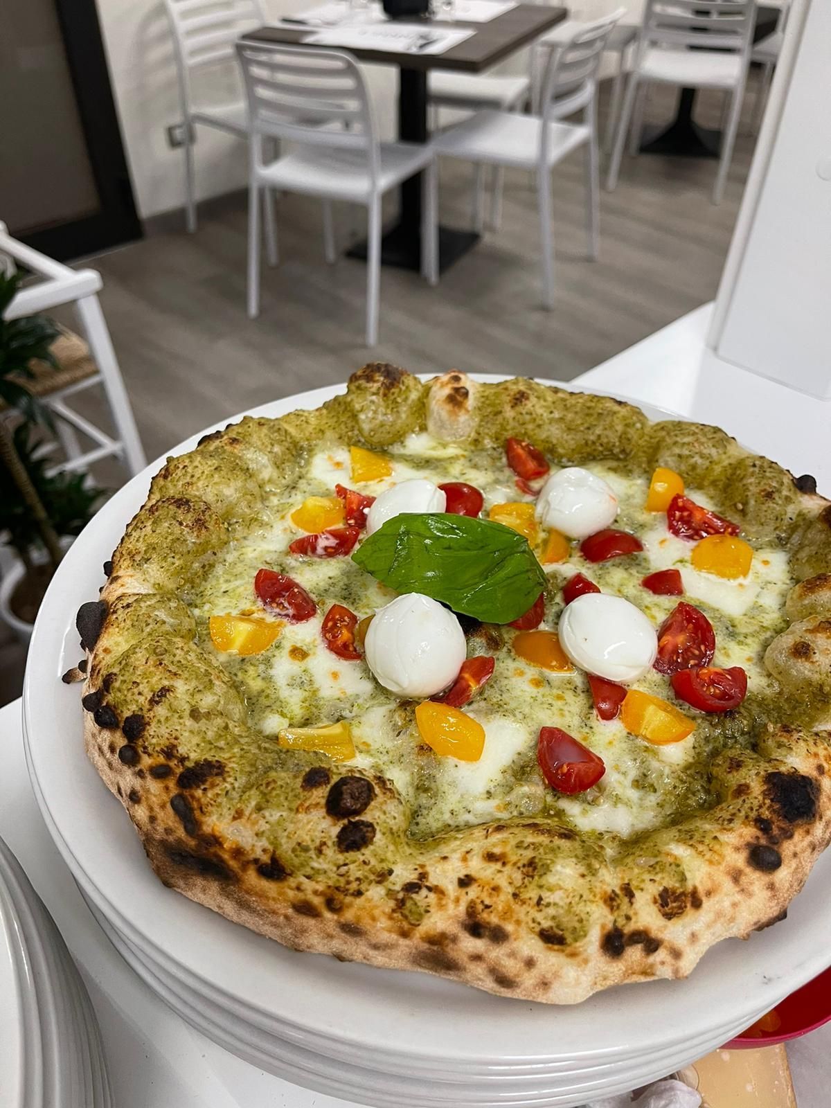 Una pizza con salsa al pesto verde, pomodorini gialli e rossi e palline di mozzarella fresca, servita in un ristorante.