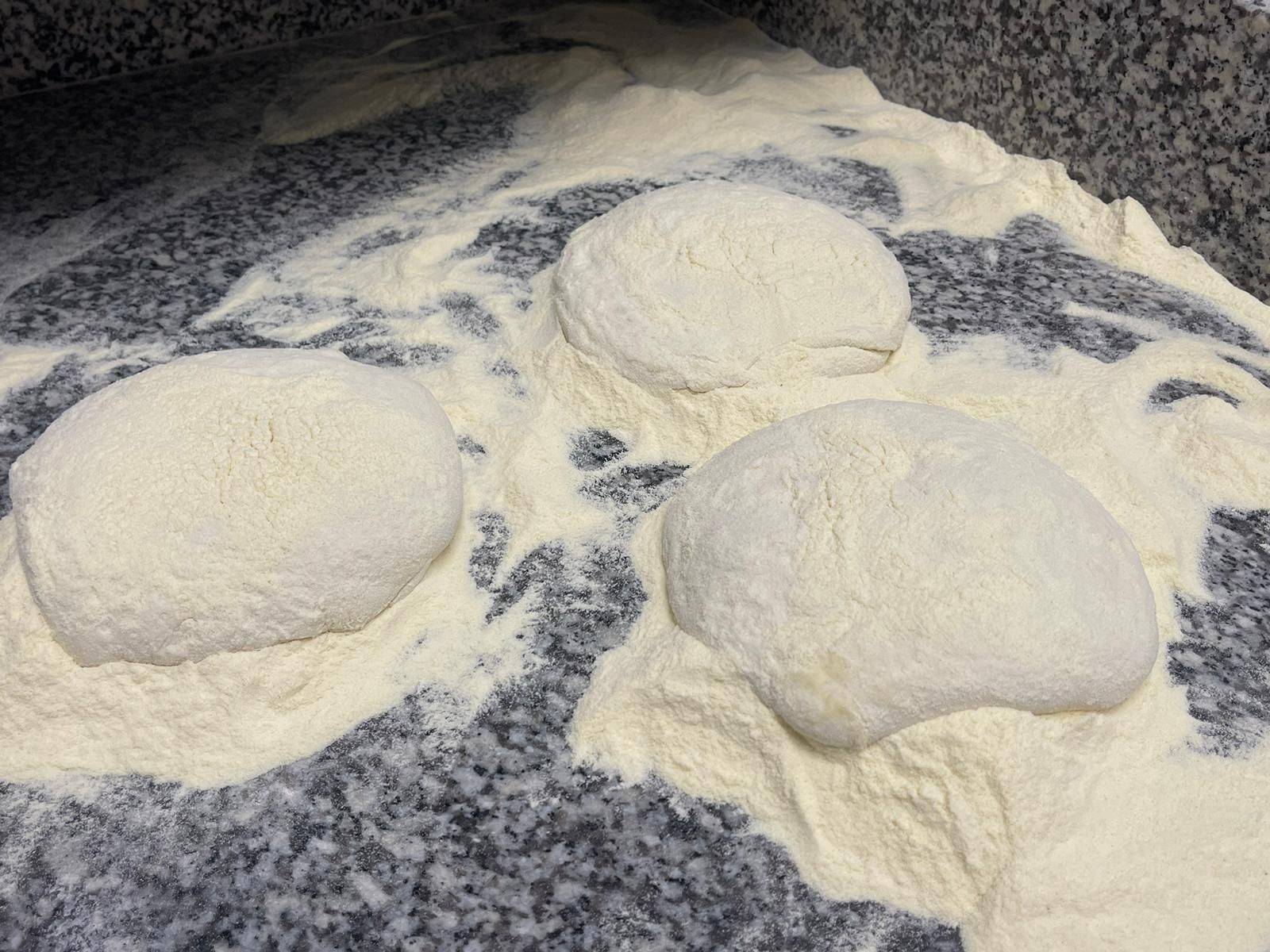 Tre palline rotonde di impasto per pizza infarinate, appoggiate su un piano di lavoro in granito.