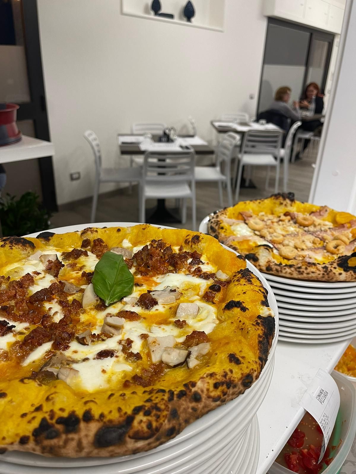In un ristorante, due pizze artigianali con crosta dorata e condimenti cremosi sono disposte su piatti impilati.