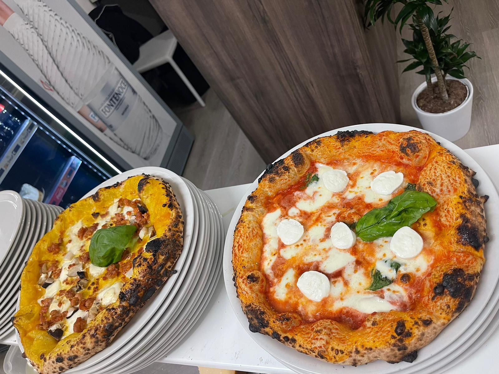 Due pizze artigianali con crosta croccante, una condita con formaggio e basilico, l'altra con una base di salsa gialla.