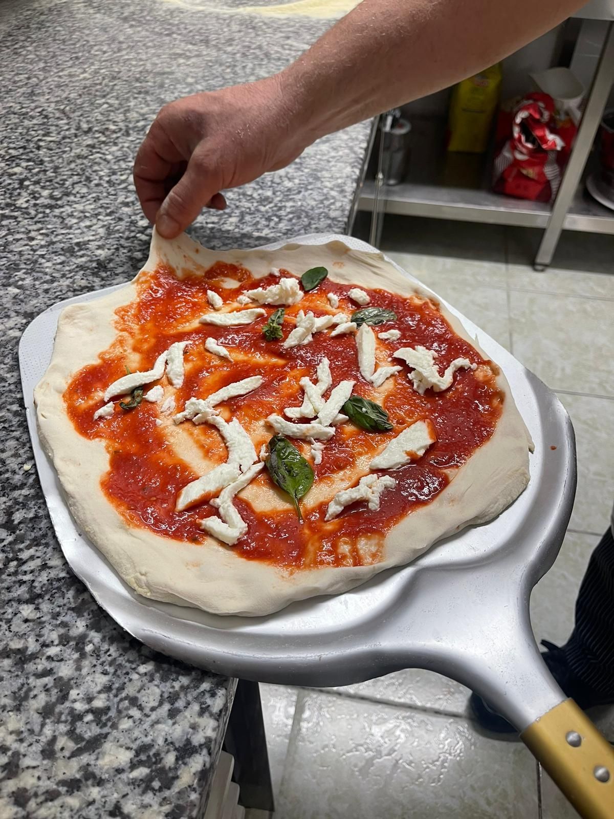 In cucina, una pala di metallo per preparare una pizza condita con salsa di pomodoro, strisce di mozzarella e basilico.