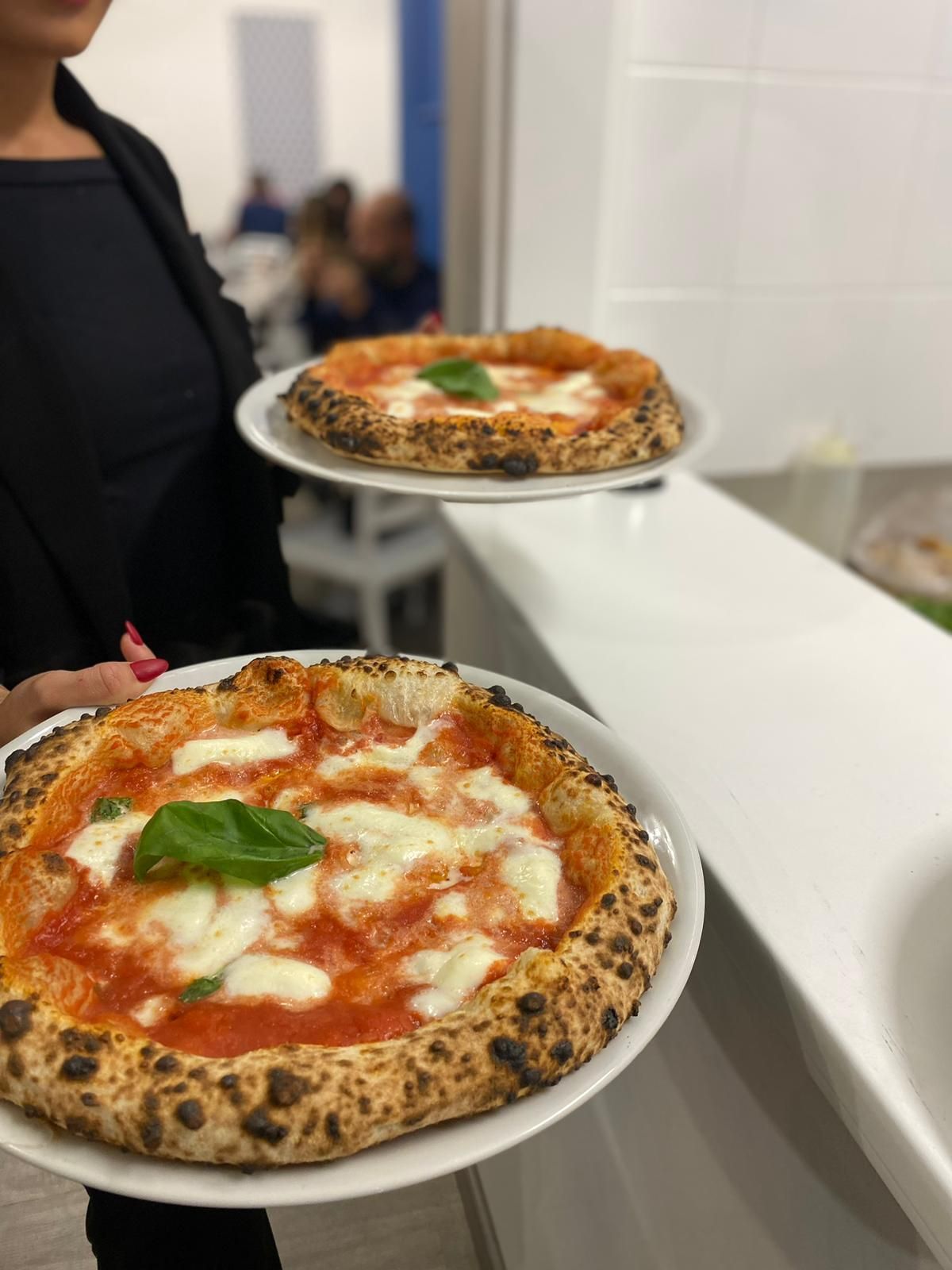 Una persona tiene in mano due piatti, ognuno dei quali presenta una pizza Margherita appena sfornata  con basilico.