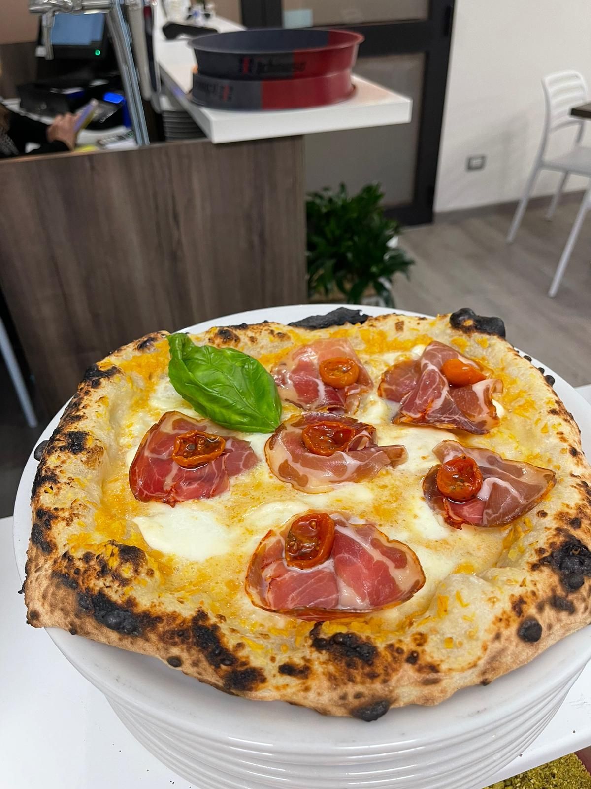 Una pizza condita con formaggio fuso, sottili fette di salumi, pomodorini arrostiti e una foglia di basilico fresco.