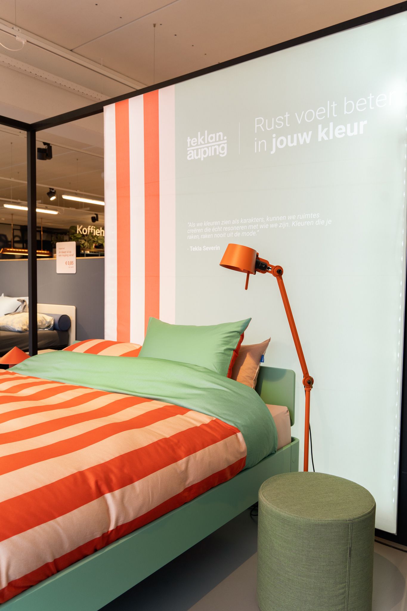 Een opgezette slaapkamer met oranje en wit gestreept beddengoed, een groen bedframe en een oranje lamp.