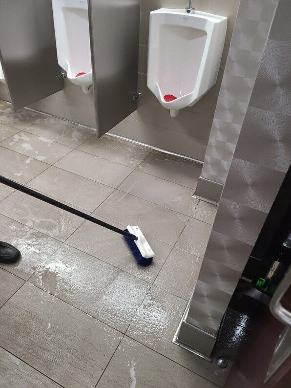 Mop on wet tiled restroom floor between urinals and a stall partition