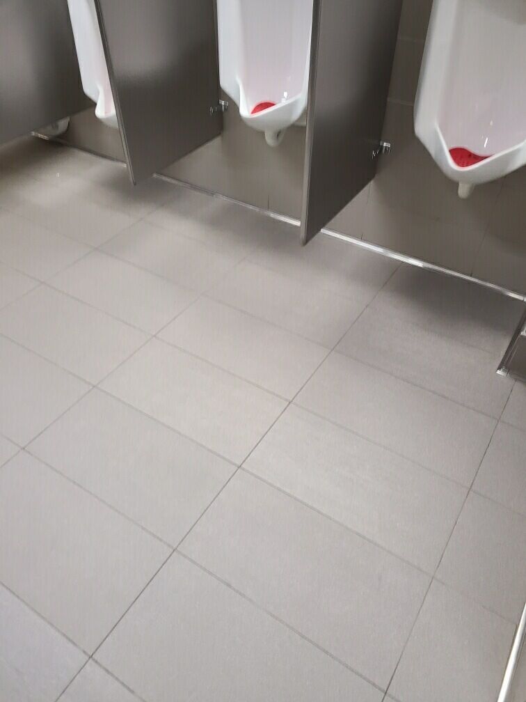 Empty restroom with gray tile floor and white urinals against a dark partition wall.