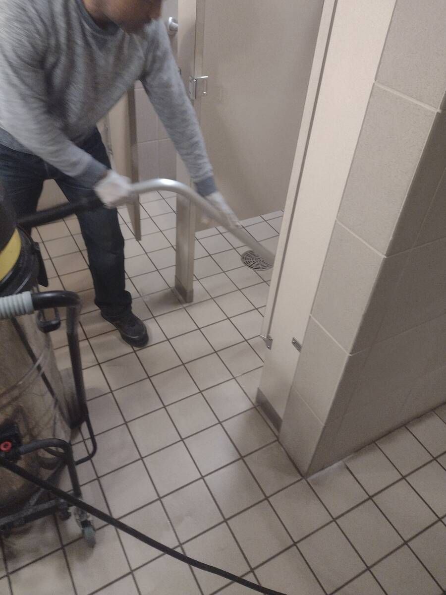 Person using a vacuum cleaner on a tiled floor in a hallway or bathroom.