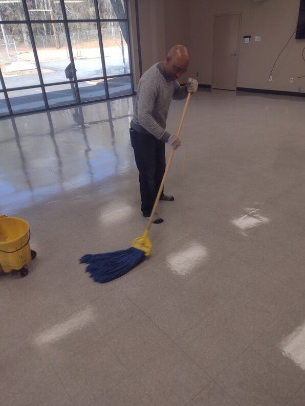 Person mopping a shiny floor in a large empty room with large windows.