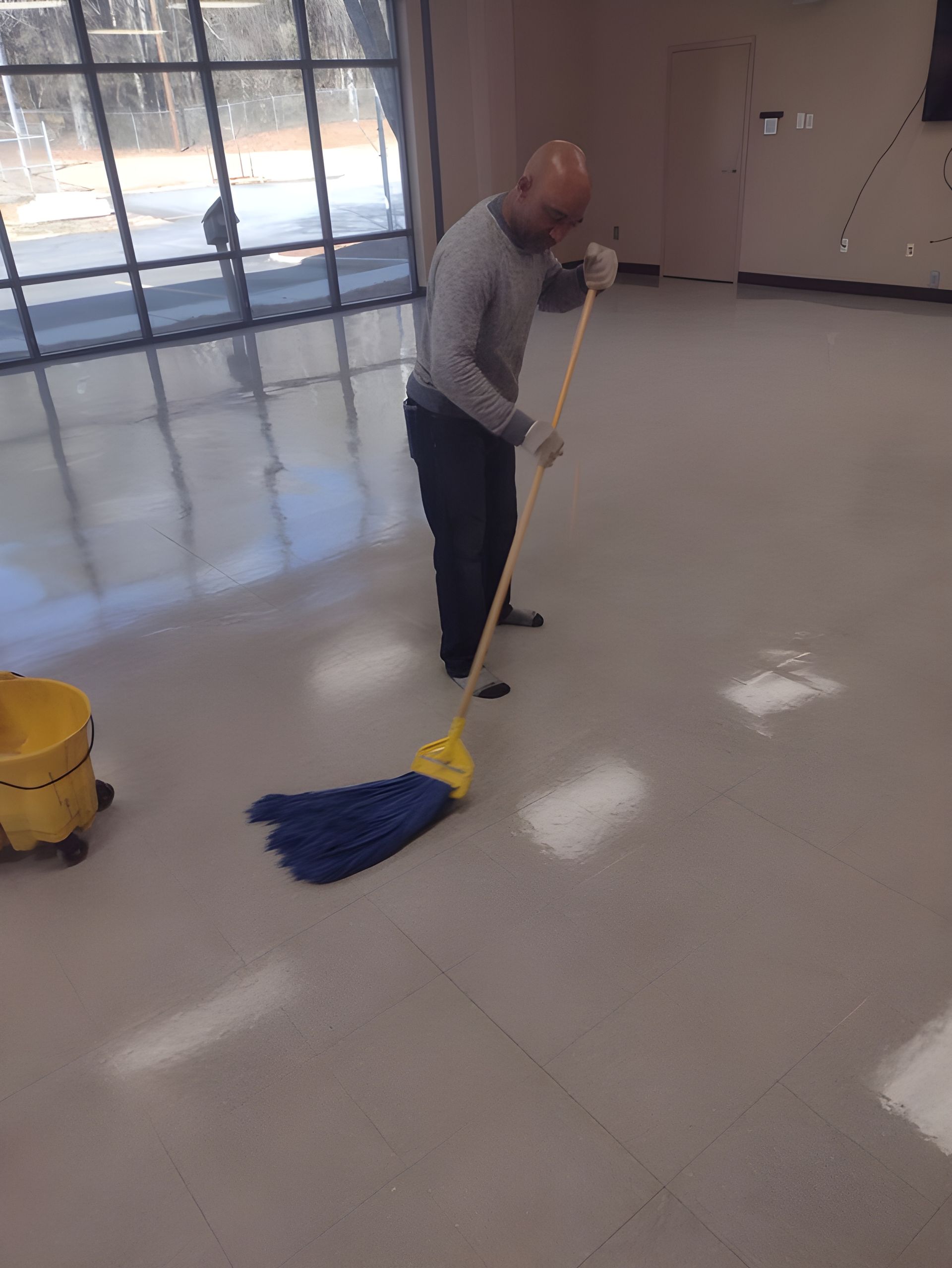 Person mopping a shiny floor in a large empty room with windows.