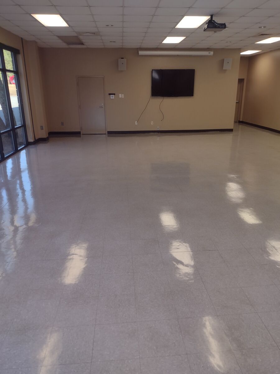 Empty beige room with tiled floor, wall-mounted TV, and doors along the back wall