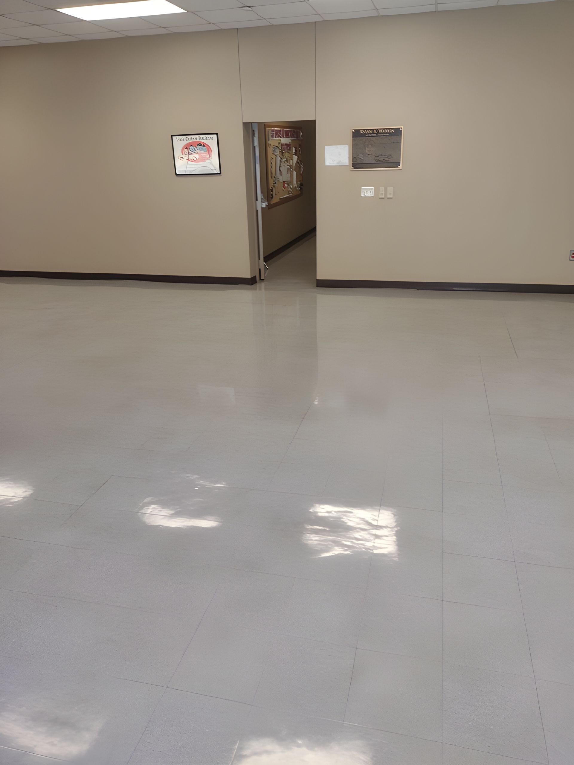 Empty beige hallway with a doorway, wall signs, and a polished gray floor.