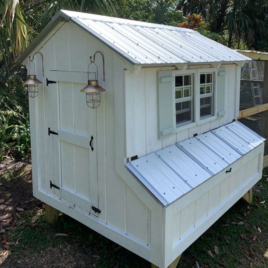 A white chicken coop with a metal roof and shutters